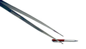 A large pair of tweezers grabs at a pen on the ground, the pen provides perspective for the large size of the tweezers