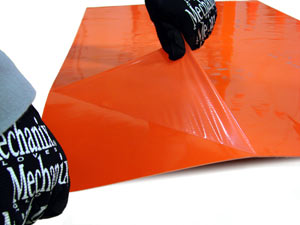 An orange sticky mat with a layer being removed by a pair of gloved hands